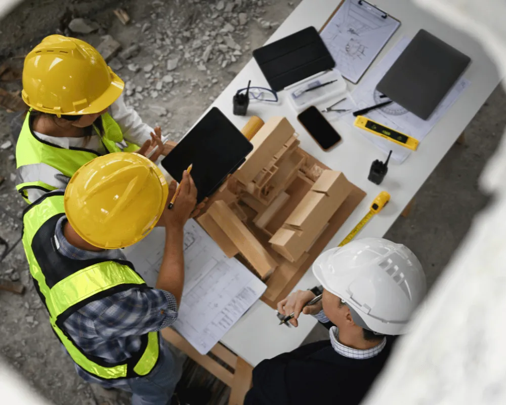 Partners and clients: engineers reviewing plans and a scale model at a project site